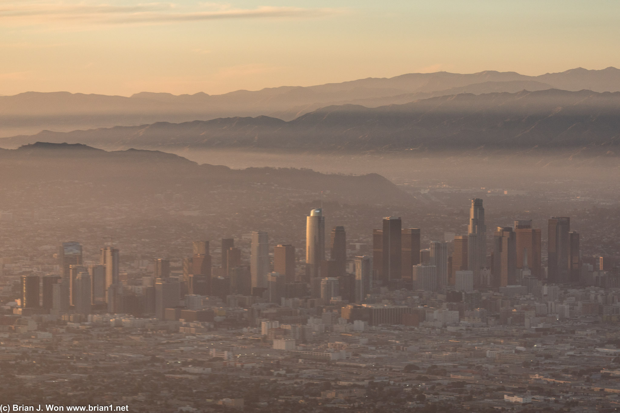 The sun sets through the fog over downtown Los Angeles.