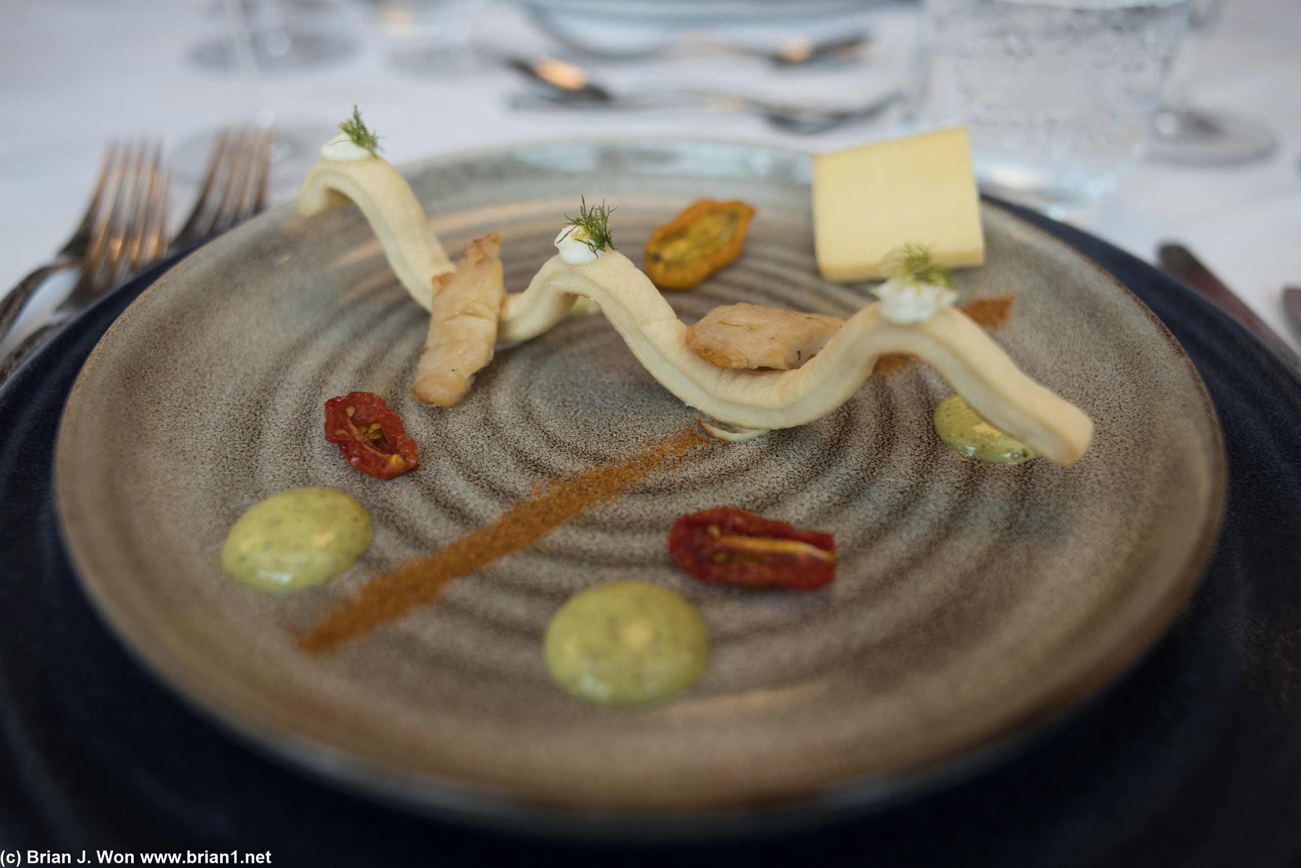 Smoked lionfish, cherry tomato, mayo, tomato powder, lemon, cheese, cracker in the shape of a wave.